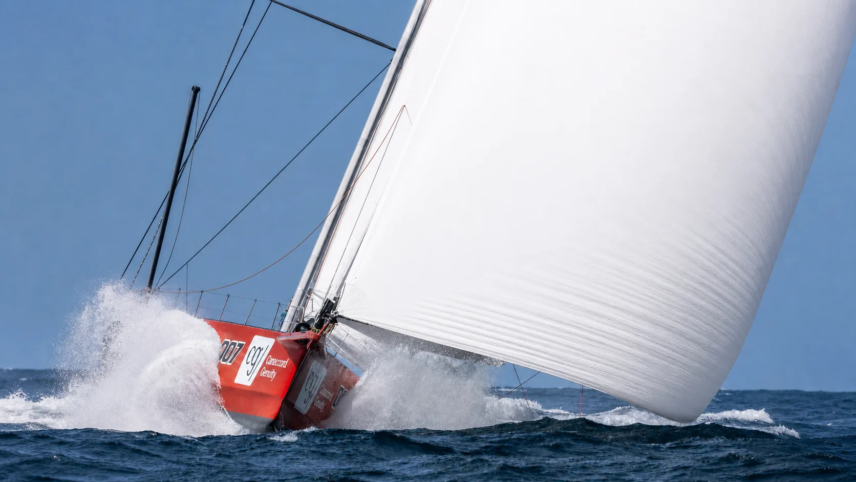 Racing yacht driving through waves under a loaded white sail